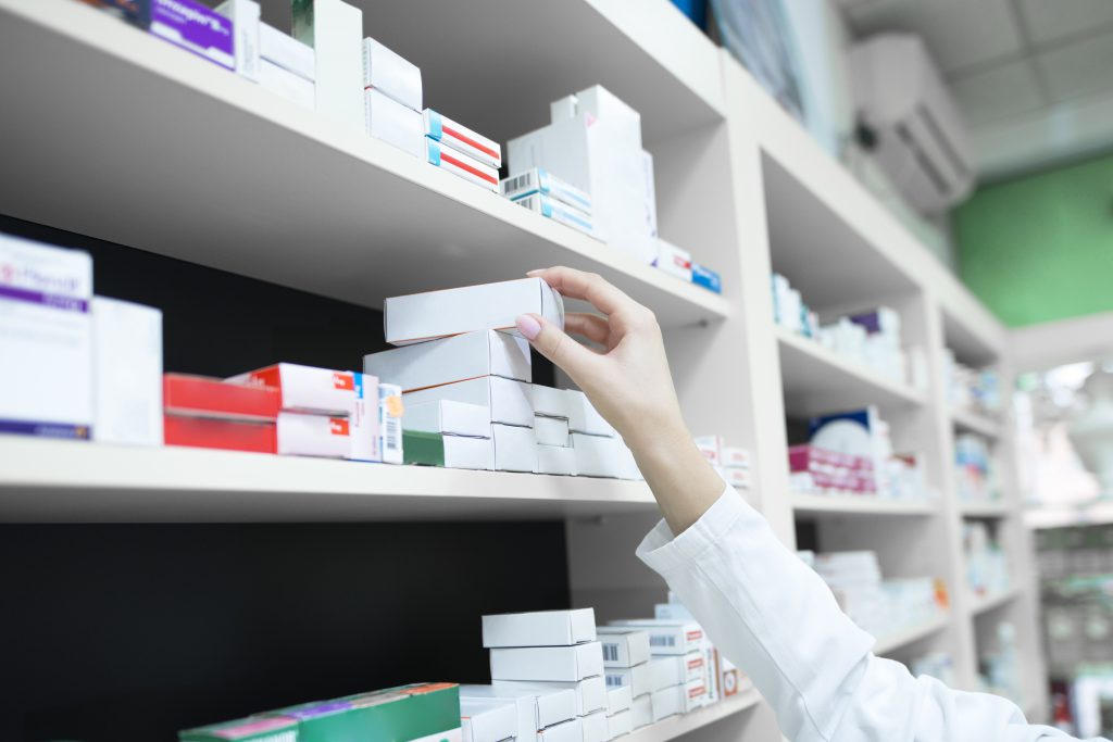 Closeup View Of Pharmacist Hand Taking Medicine Box From The Shelf In Drug Store.