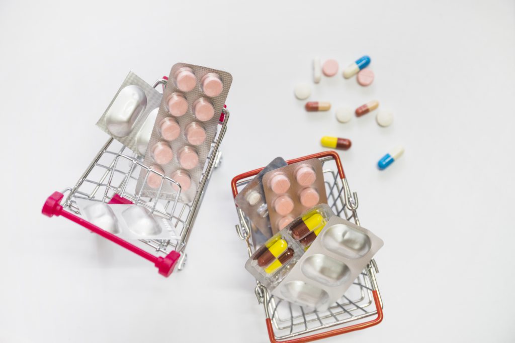 Two Miniature Shopping Carts Filled With Pills Blister White Background