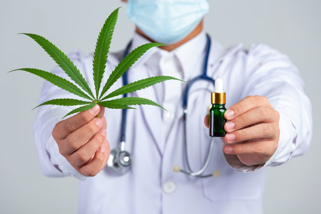 Medical Doctor Holding Cannabis Leaf And Bottle Of Cannabis Oil